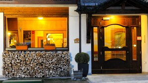 A building with a wooden facade, a stack of firewood, and a black door with glass panels. - Hotel Montana (Pinzolo)