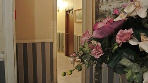 A hallway with striped walls, a door, and a large floral arrangement. - Hotel Assisi (Rome)