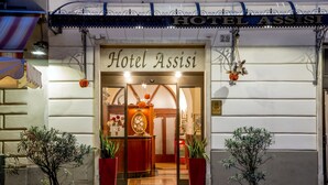 Hotel Assisi's entrance with a sign, potted plants, and a warm interior visible through the doorway. - Hotel Assisi (Rome)