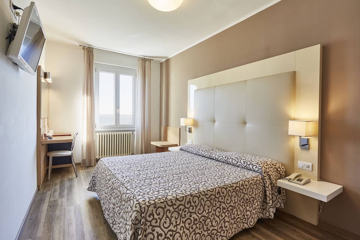 Een hotelkamer met een groot bed, een bureau, een stoel, een aan de muur bevestigde televisie en een raam met gordijnen.