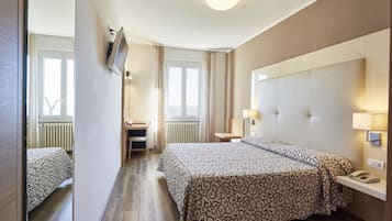 Habitación de hotel con una cama grande, un escritorio, una silla y un televisor montado en la pared.