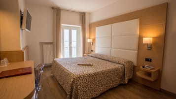 Habitación de hotel con cama, mesita de noche, lámpara y vistas al exterior.