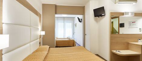 A hotel room with a large bed, a bedside table, a mirror, a TV, and an air conditioning unit.