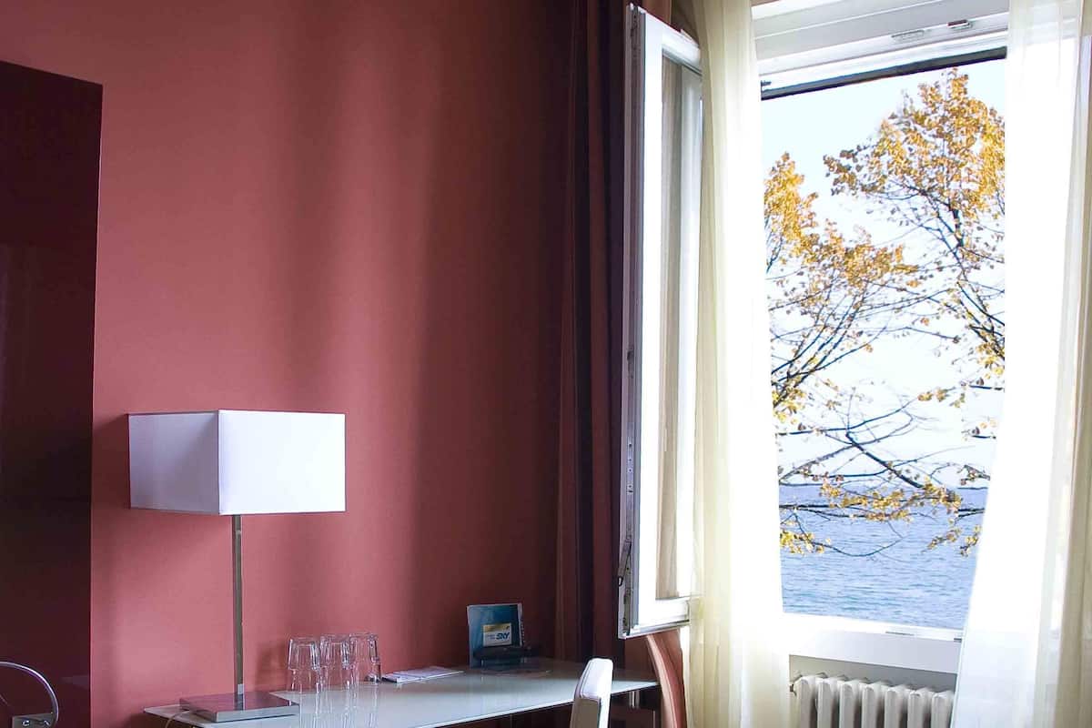 Een hotelkamer met een bureau, stoel, lamp en uitzicht op een meer door een raam.