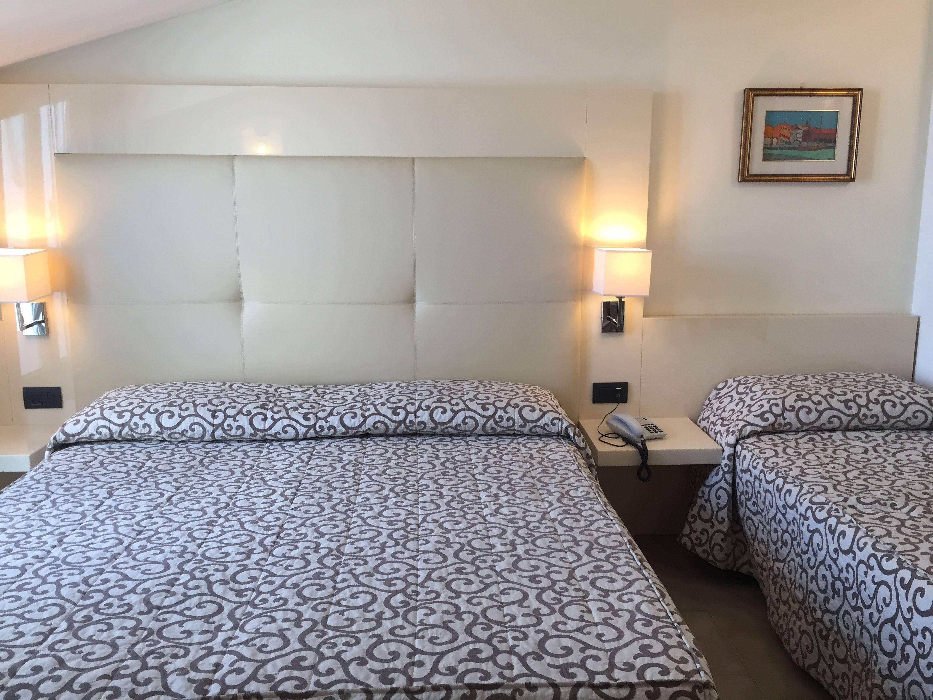 Habitación de hotel con dos camas, cabeceros, lámparas de noche, teléfono y un cuadro en la pared.