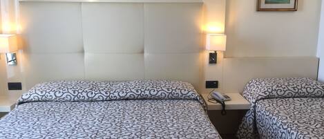 Habitación de hotel con dos camas, cabeceros, lámparas de noche, teléfono y un cuadro en la pared.