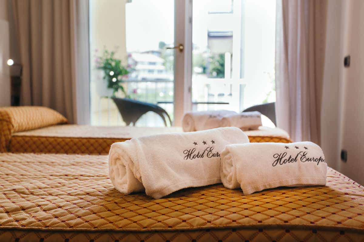 Een hotelkamer met twee bedden, elk met een gewatteerde matras en een opgerolde handdoek met de tekst 'Hotel Europa'.