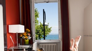 Une chambre avec un lit, une fenêtre avec des rideaux, une lampe et une vue sur la mer.