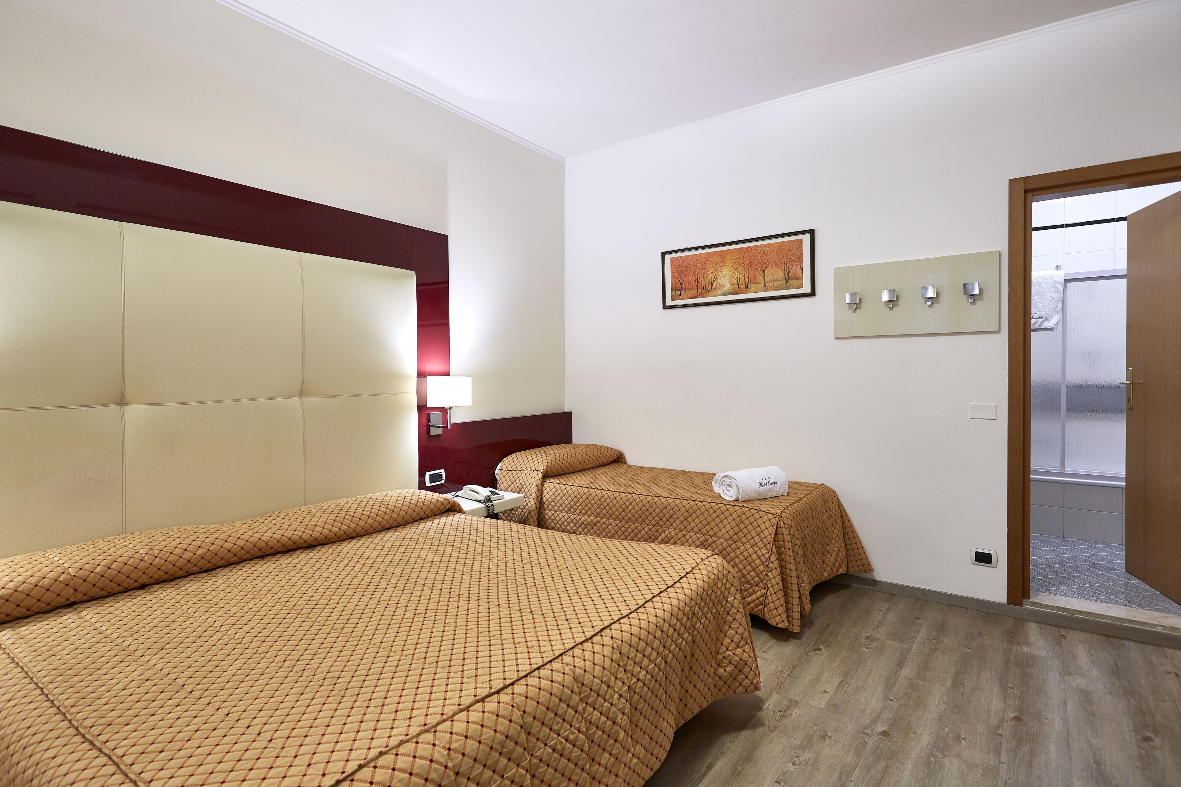 Een hotelkamer met twee bedden, een hoofdeinde, een nachtkastje, een lamp, een schilderij en een deur naar een badkamer.