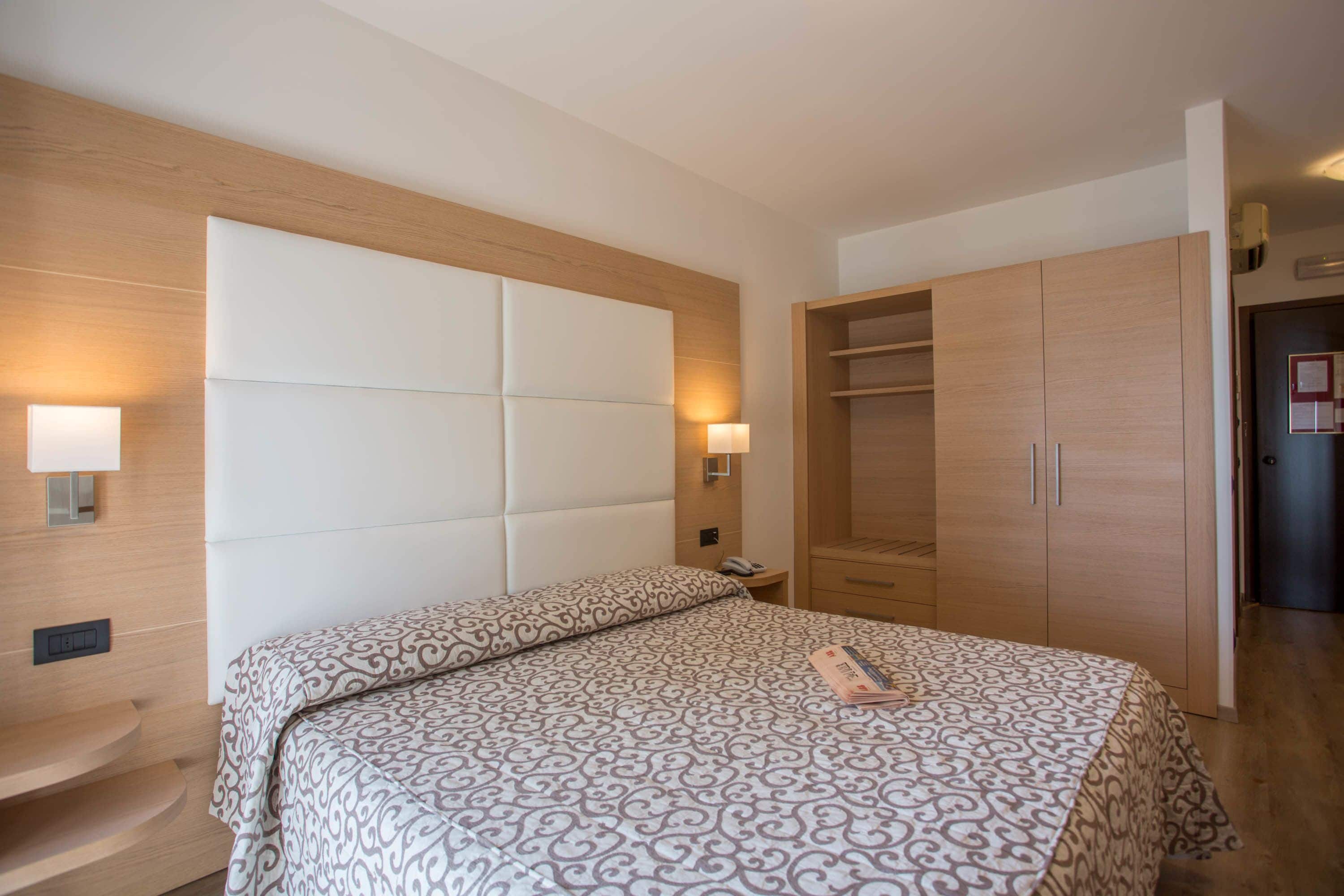 Un dormitorio con cama, lámparas de noche, un armario de madera y una mesita de noche.