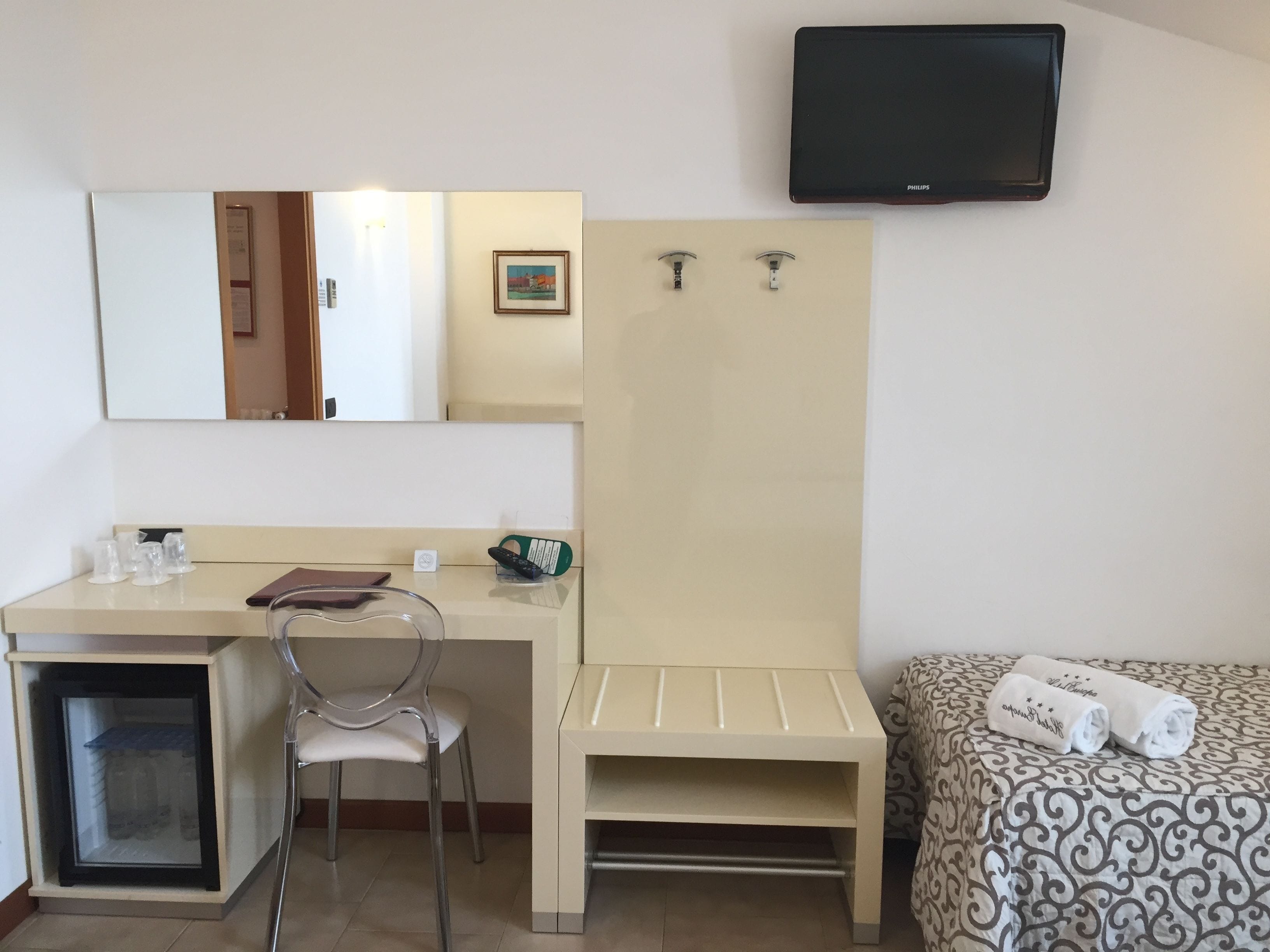 Habitación de hotel con escritorio, silla, televisor, cama y un mueble bajo.