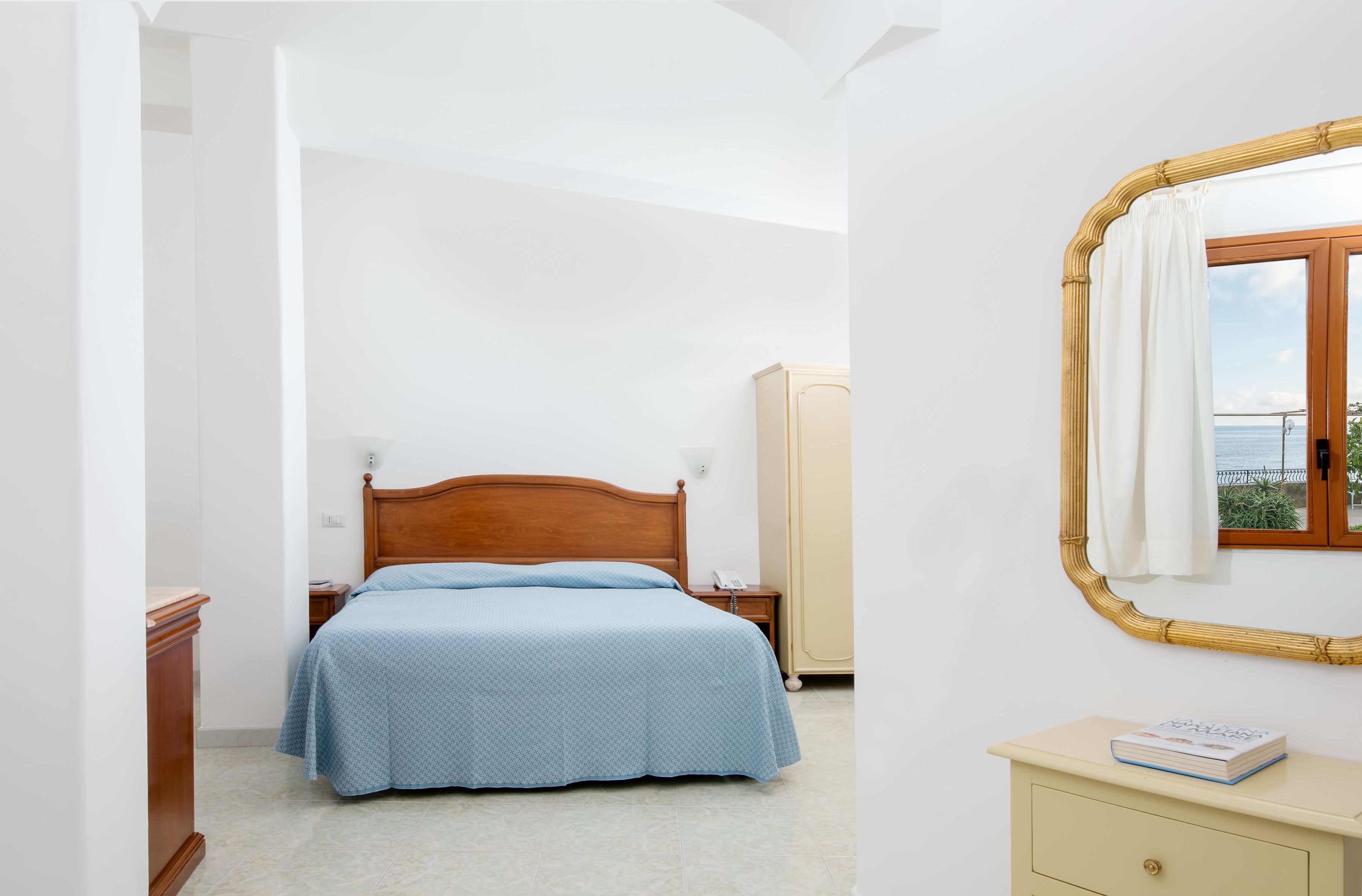 Una camera da letto con un letto di legno, un comodino, un armadio e uno specchio con vista mare.