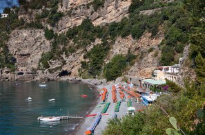 Una zona costera con barcos amarrados a la orilla, un acantilado rocoso y edificios de estilo arquitectónico mediterráneo.