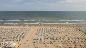 A beach with rows of umbrellas and sun loungers, a lifeguard tower, and the ocean in the background.