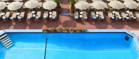 Un área de piscina con múltiples tumbonas y sombrillas, rodeada por un camino empedrado.