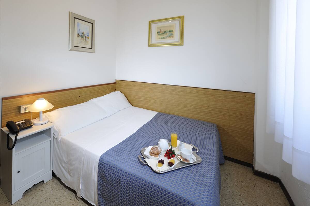 Een hotelkamer met een net opgemaakt bed, een nachtkastje met lamp en telefoon, en een dienblad met ontbijtartikelen.