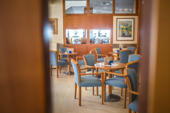 Un restaurante con mesas redondas y sillas tapizadas en azul, obras de arte enmarcadas en las paredes y vistas amplias a través de grandes ventanales.