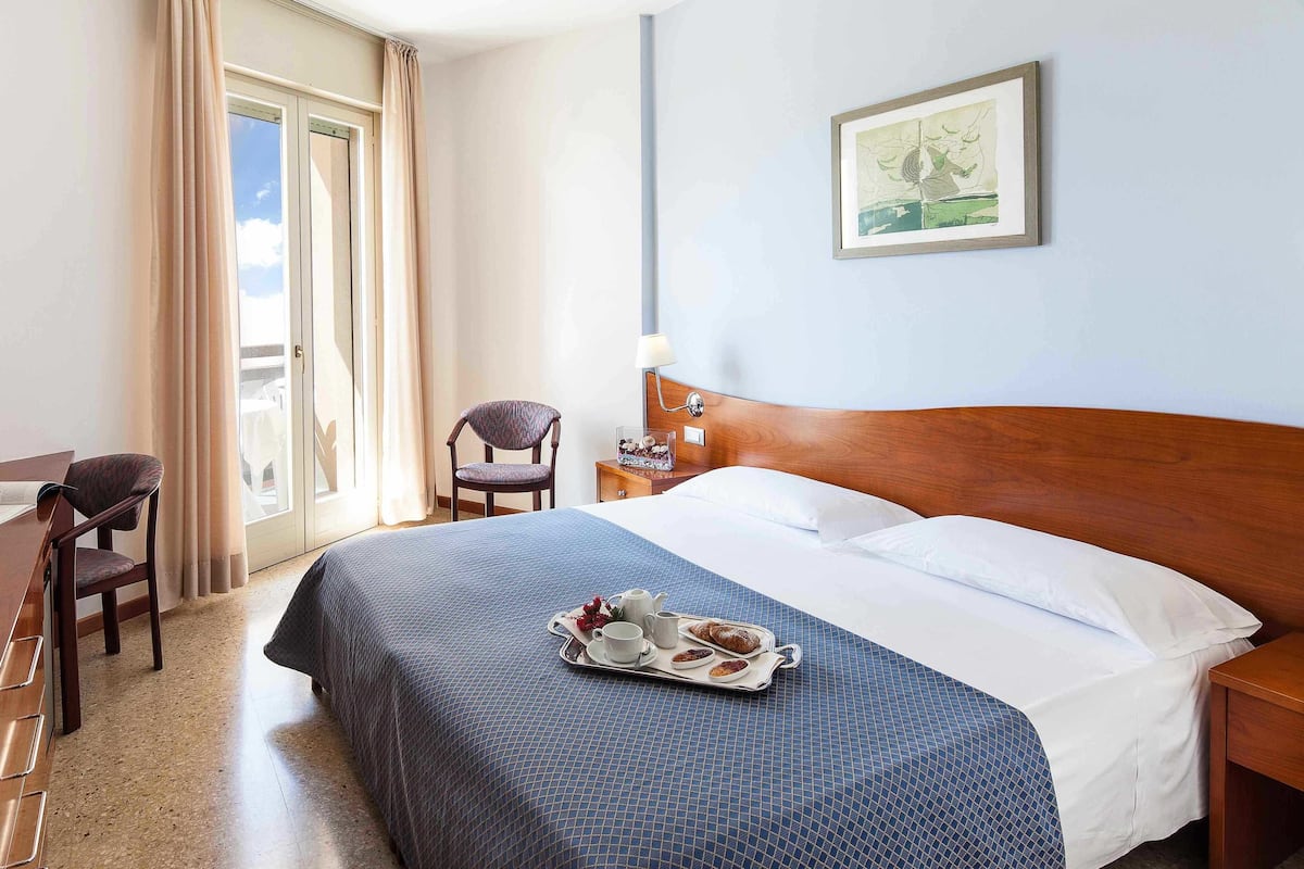 Een hotelkamer met een bed, een stoel, een bureau, een lamp en een schilderij aan de muur.