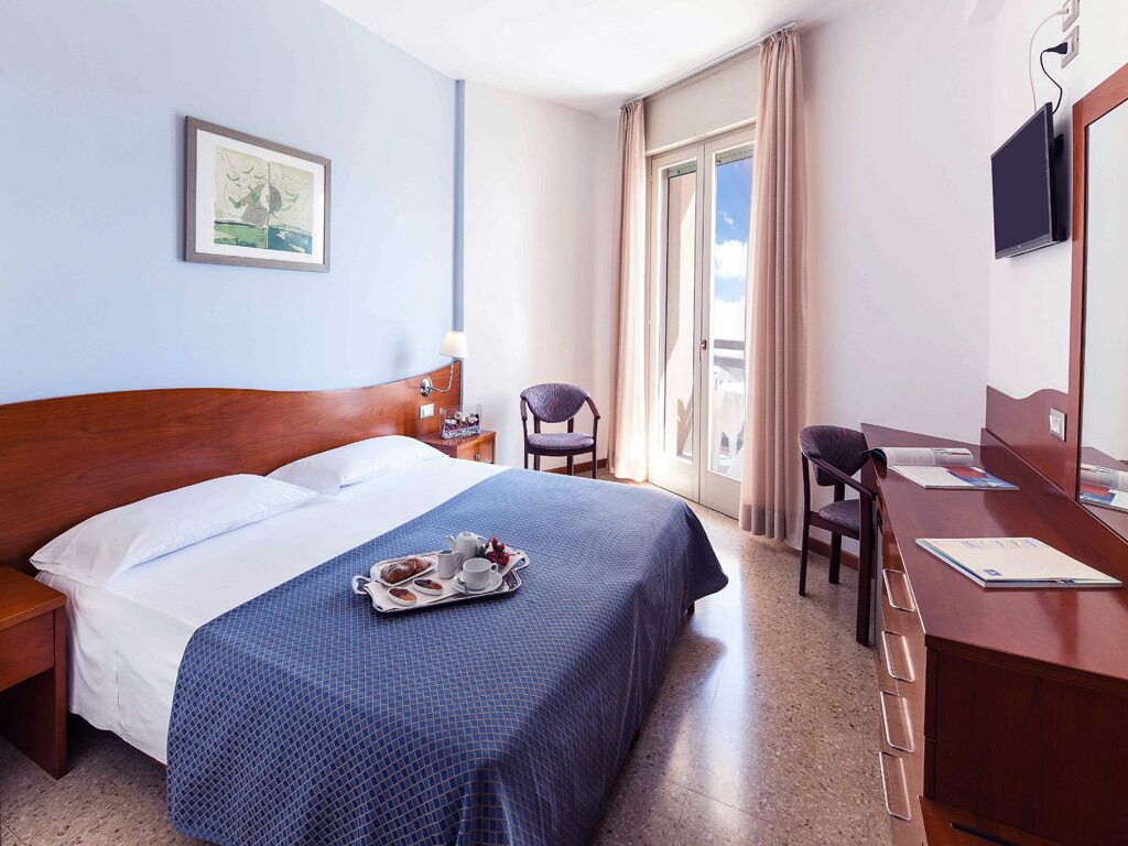 Hotelkamer met een bed, bureau, stoel, televisie en een raam met gordijnen.