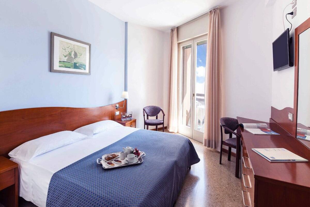 Hotelkamer met een bed, bureau, stoel, televisie en een raam met gordijnen.