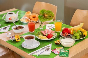 A breakfast table with various food items, a teapot, and a glass of orange juice. - Hotel dei Mille (Rome)