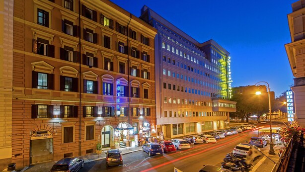 A multi-story hotel with a classic facade, a ground-level entrance, and a parking area with cars. - Hotel dei Mille (Rome)