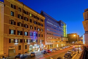 A multi-story hotel with a classic facade, a ground-level entrance, and a parking area with cars. - Hotel dei Mille (Rome)