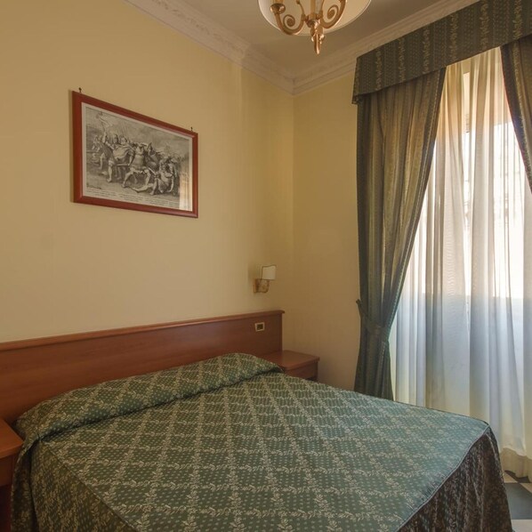 Habitación de hotel con cama, mesita de noche, lámpara, un cuadro en la pared y ventana con cortinas.