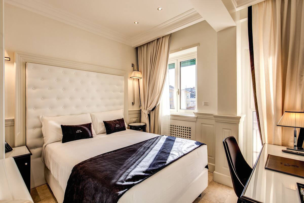 Una habitación de hotel con una cama grande, un escritorio con lámpara y una ventana con cortinas.