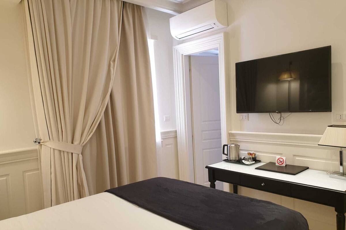 Una habitación de hotel con cama, escritorio con televisor, lámpara y cafetera.