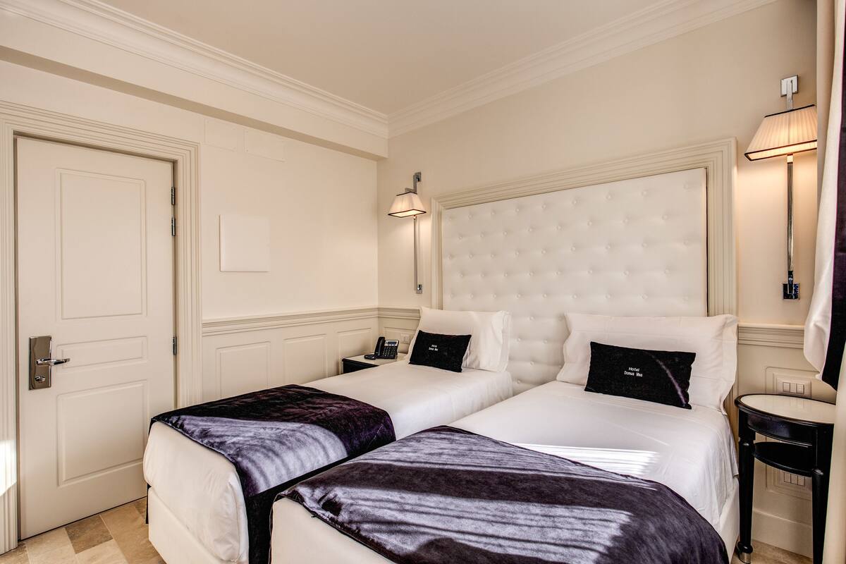 Una habitación de hotel con dos camas, una mesita de noche, una lámpara y un espejo.