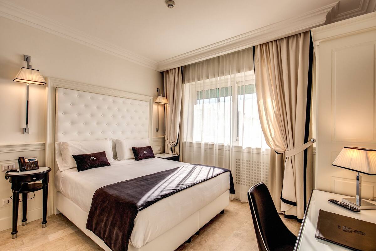 Una habitación de hotel con una cama grande, lámparas de noche, un escritorio con una computadora portátil y una silla.