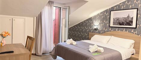 Habitación de hotel con cama, escritorio, silla, ventana con cortinas, un cuadro en la pared y suelo de madera.