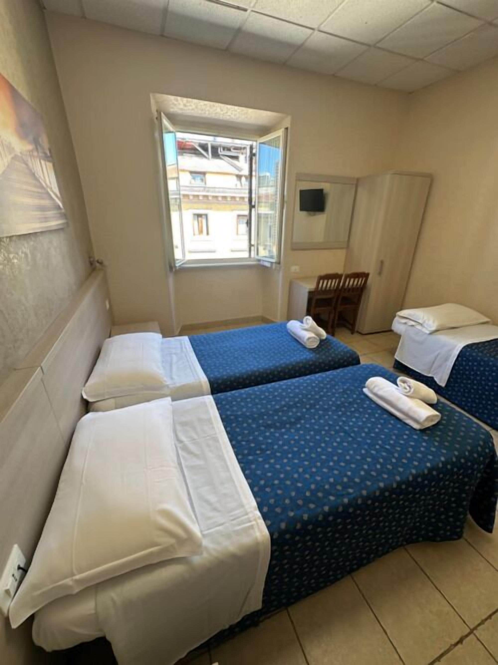 Een hotelkamer met twee bedden, een raam, een bureau en een kledingkast.