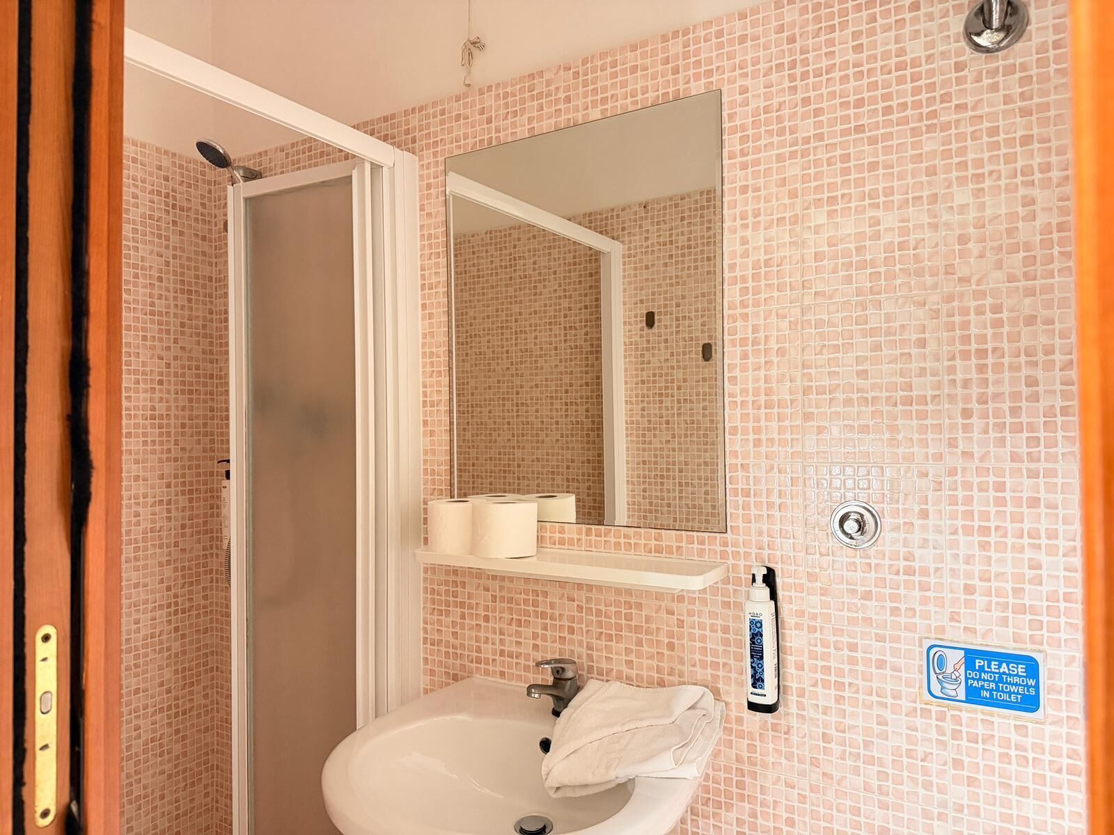 A bathroom with a sink, mirror, and toilet paper dispenser.