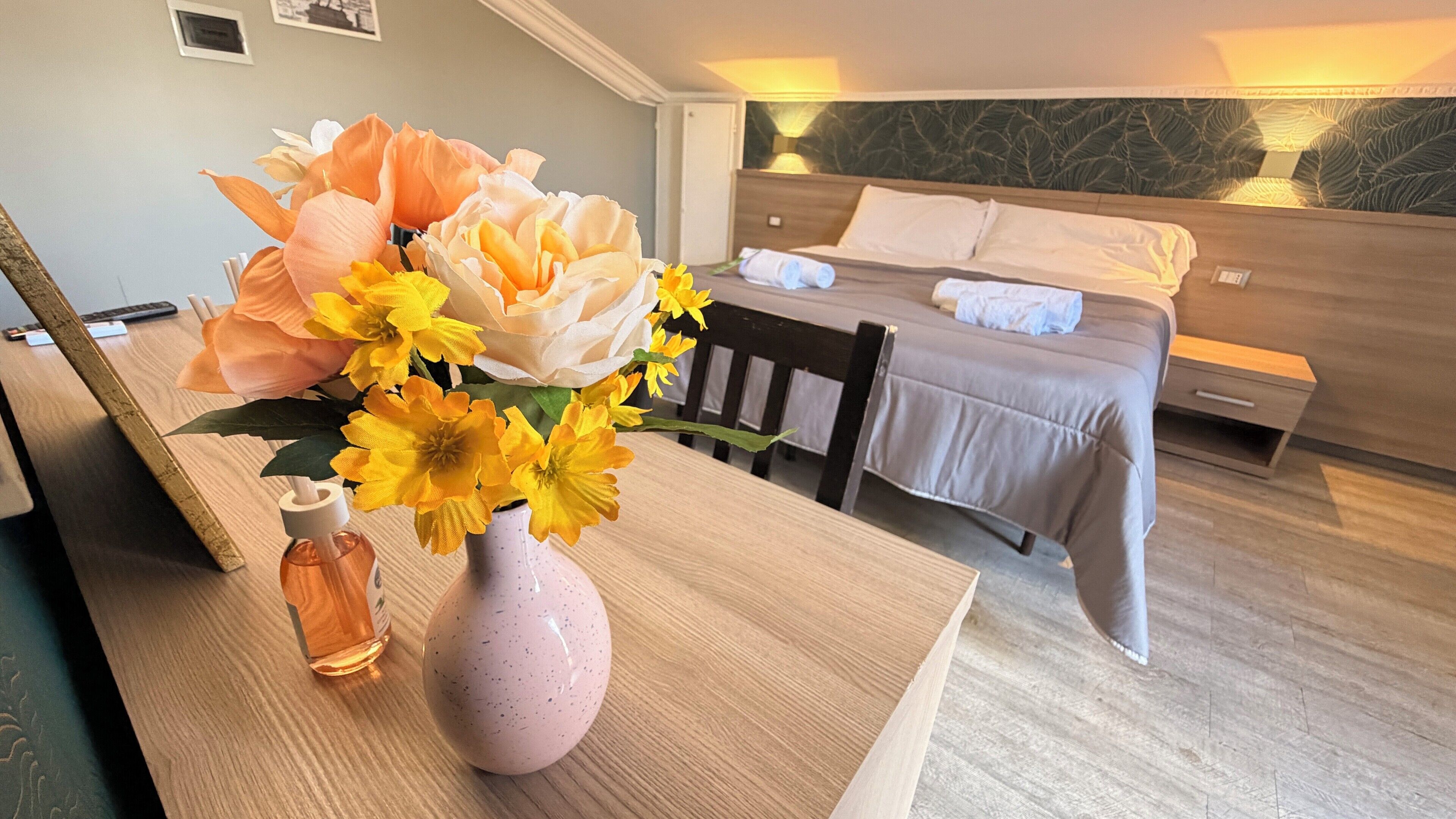 A hotel room with a bed, bedside table, and a vase with flowers.
