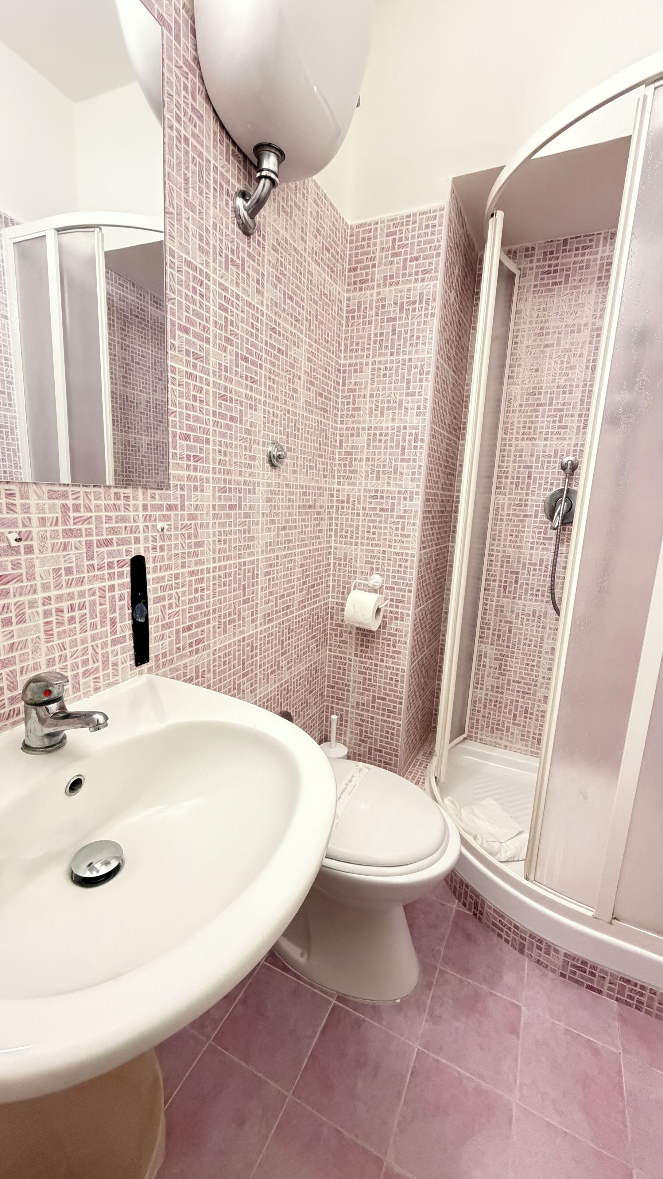 Un baño con lavamanos blanco, inodoro y ducha a ras de suelo.