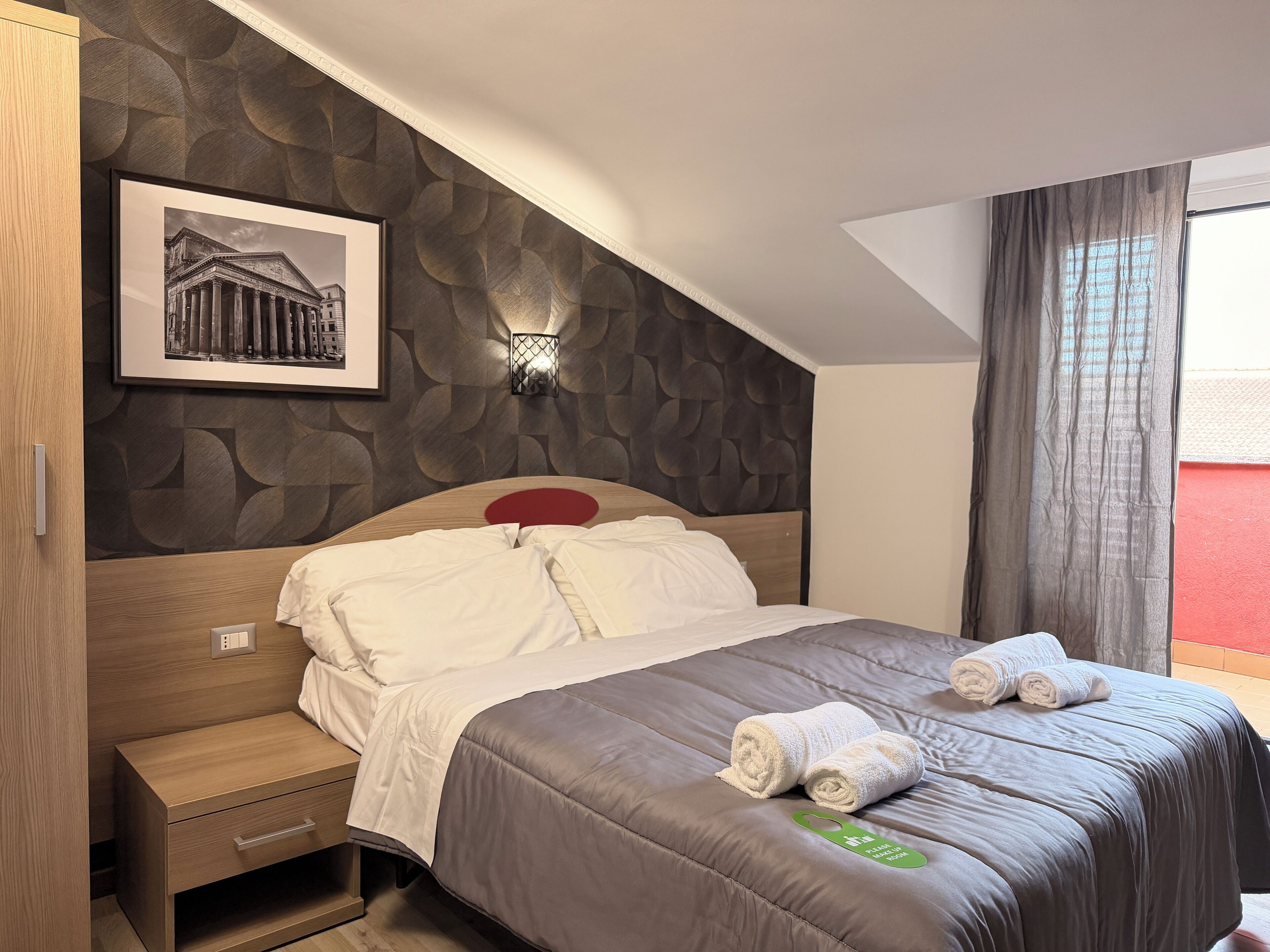 Een hotelkamer met een bed, nachtkastje, wandlamp en een ingelijst foto.