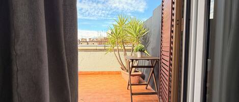 A balcony with terracotta tiles, a wooden table, and potted plants.
