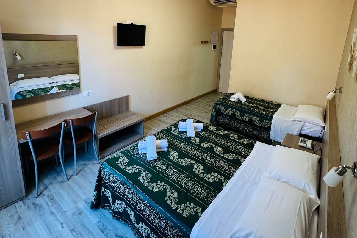 A hotel room with two beds, a desk, a chair, a TV, and an air conditioning unit.