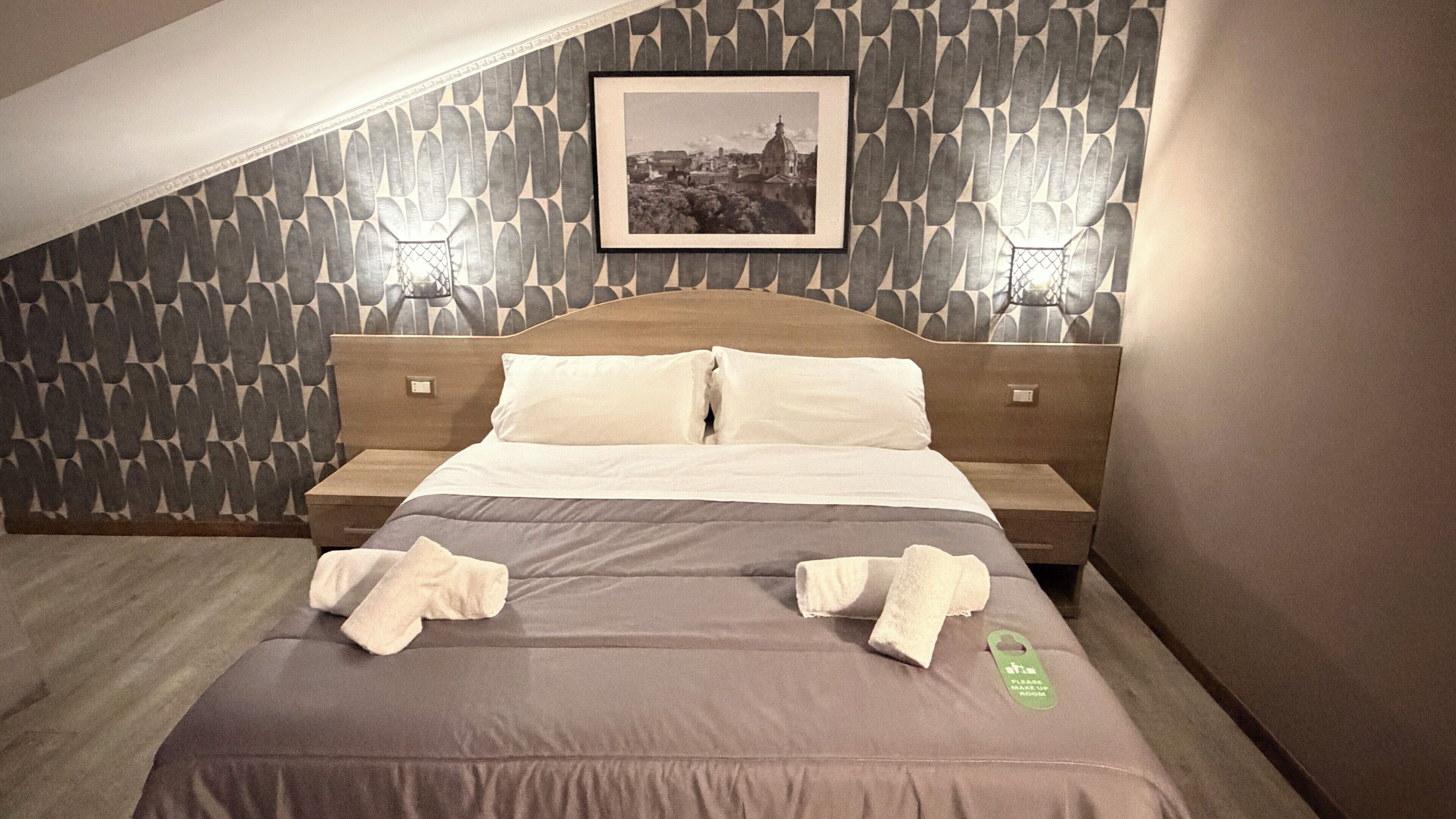 Ein Hotelzimmer mit einem Bett, zwei Nachttischen, einem gerahmten Bild an der Wand und einem Handtuch auf dem Bett.