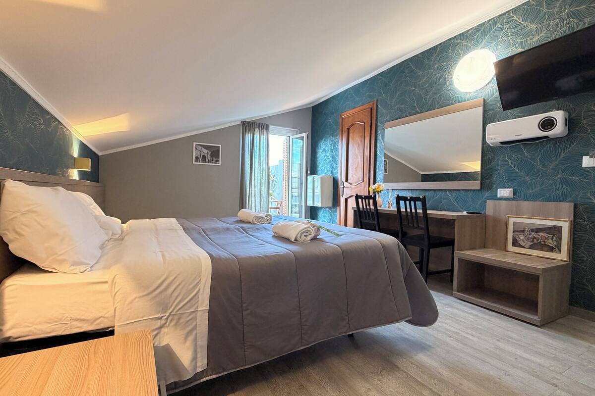 A hotel room with a bed, a desk, a chair, a mirror, and a picture frame.