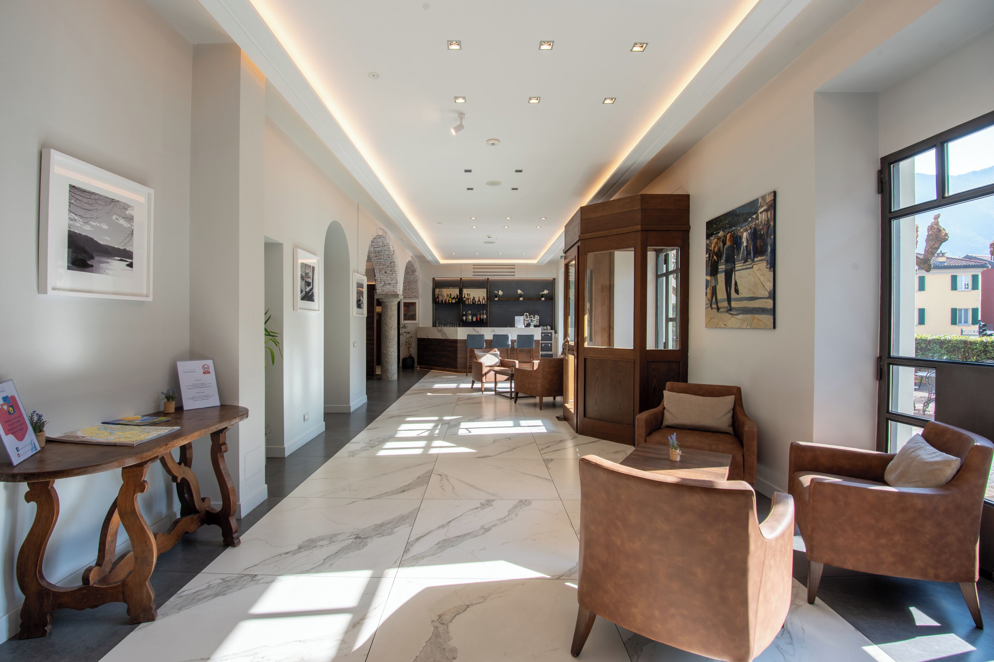Una hall d'albergo con pavimento in marmo, arredi in legno, opere d'arte incorniciate e vista attraverso ampie finestre.