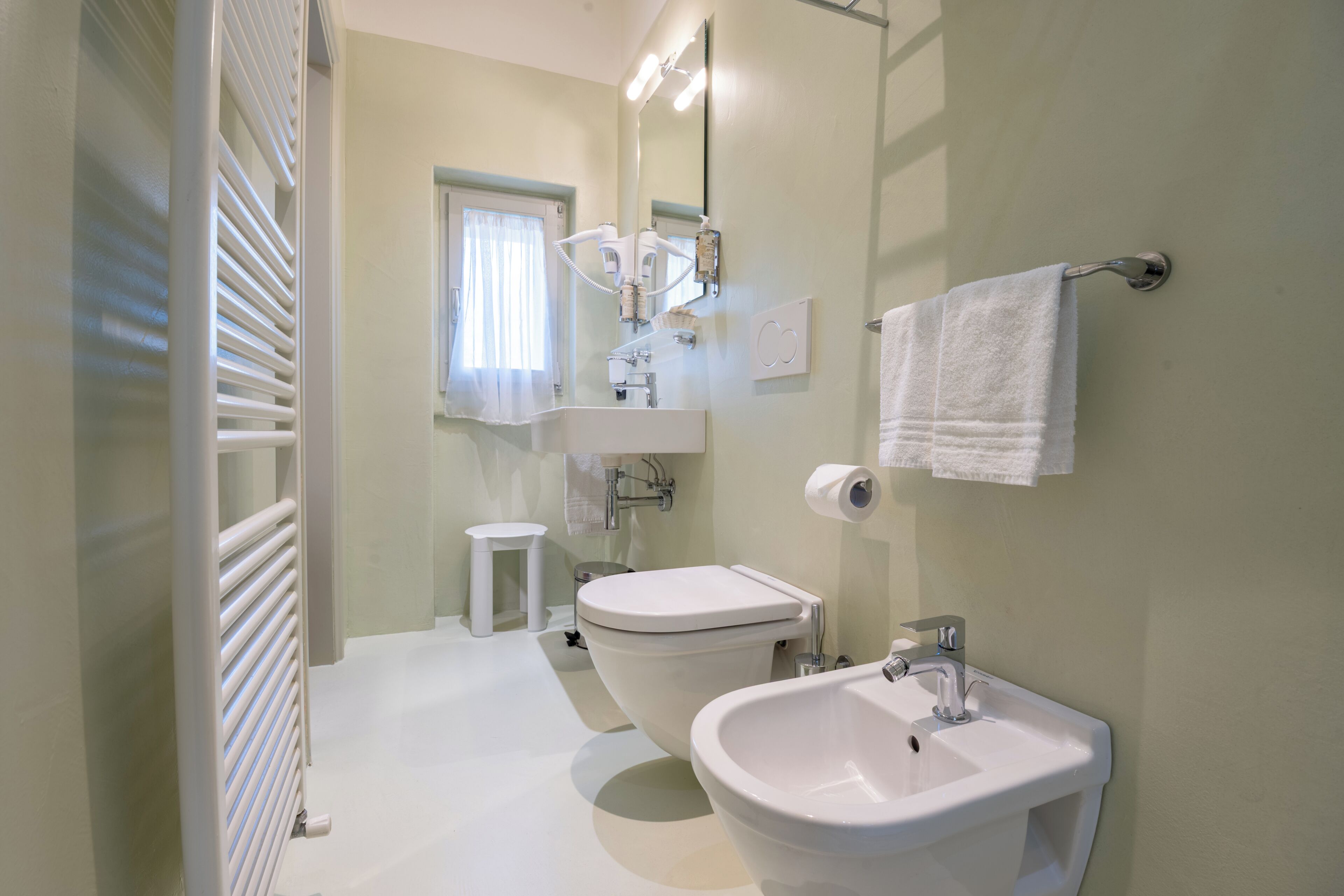 Un baño con inodoro, bidé, lavamanos y toallero.
