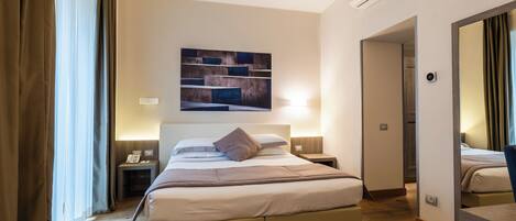 A hotel room with a large bed, bedside tables, a wall-mounted air conditioner, and a door leading to another room.