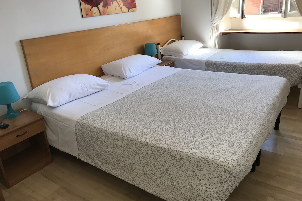 A hotel room with two beds, a wooden headboard, a nightstand with a lamp, and a painting on the wall.