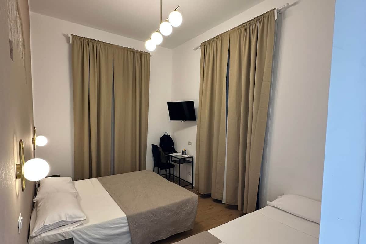 A hotel room with two beds, a desk, a chair, a TV, and a ceiling light fixture.