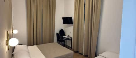 A hotel room with two beds, a desk, a chair, a TV, and a ceiling light fixture.