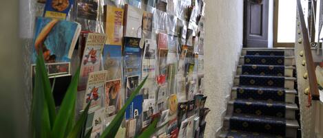 Un mur recouvert de livres et de magazines, un escalier avec une moquette à motifs et une porte ornée d’une guirlande.