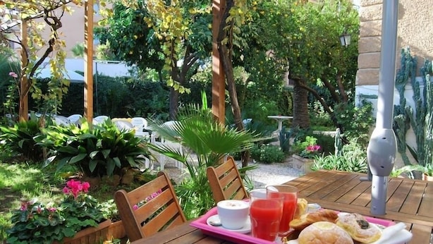 An outdoor dining area with wooden tables and chairs, surrounded by lush greenery and plants.